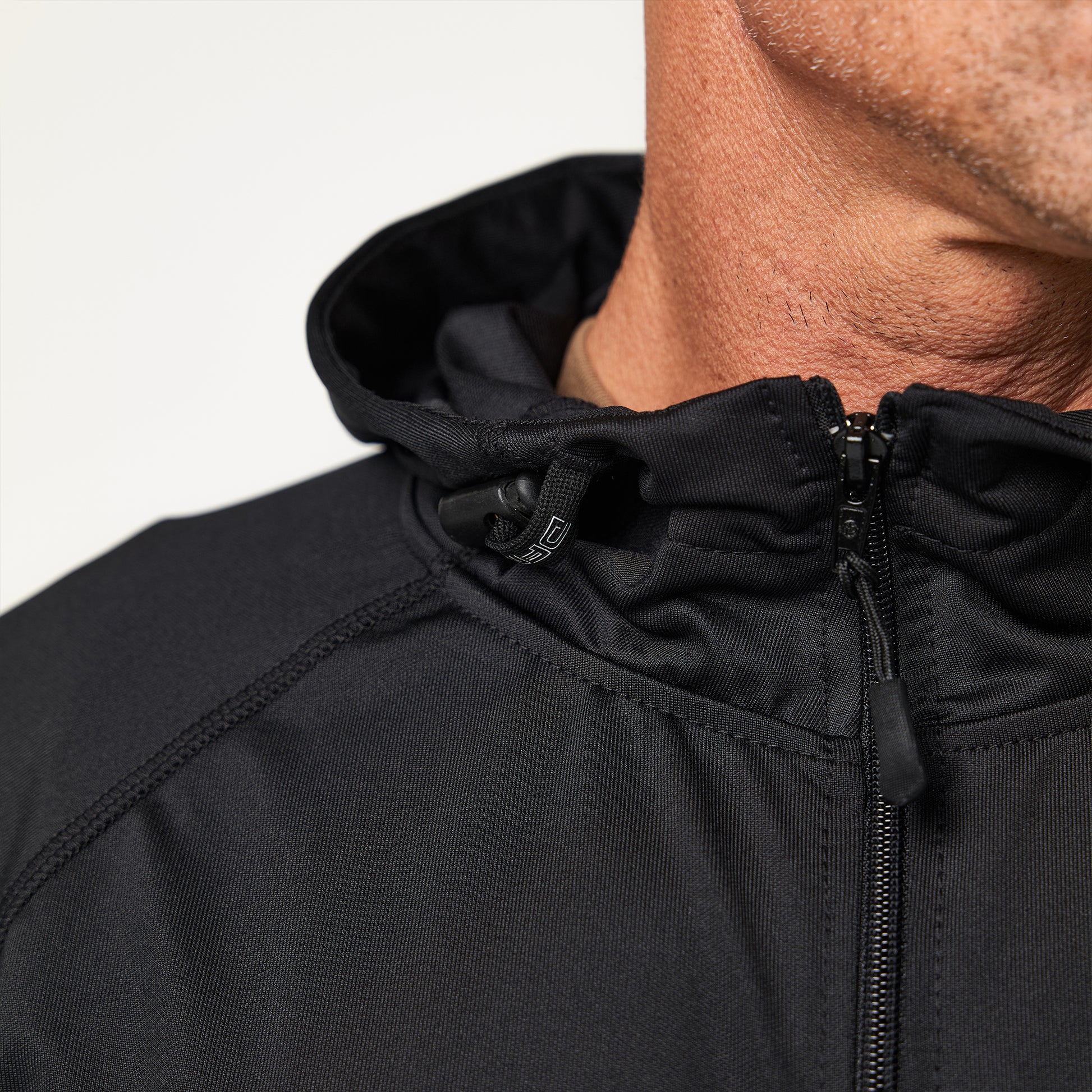 Close-up of a person wearing a black zip-up jacket with a hood. The focus is on the upper section and the jacket's fabric texture.