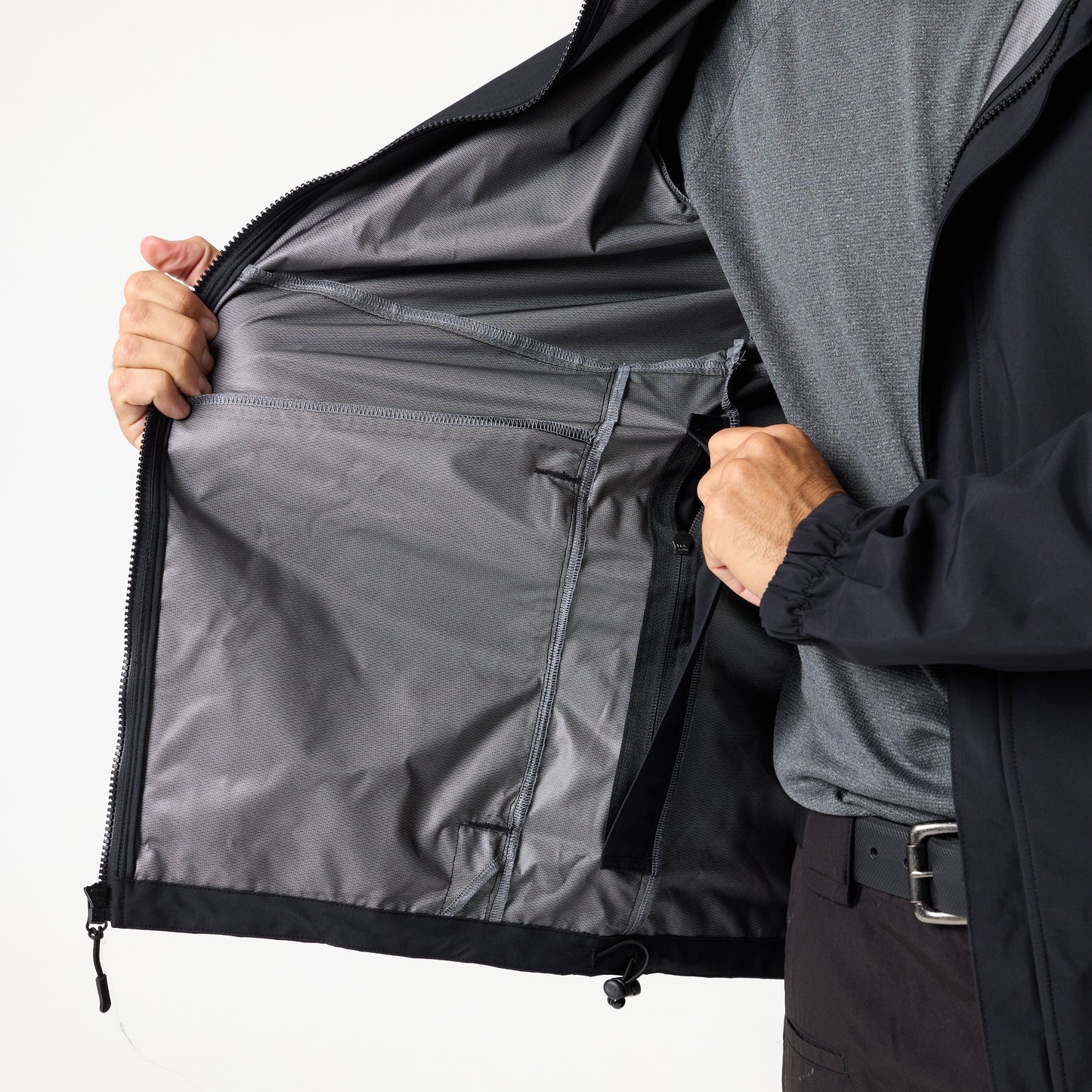 A person holds open a black DFND Assault Jacket, showing a large zippered interior pocket with mesh lining on the left side.