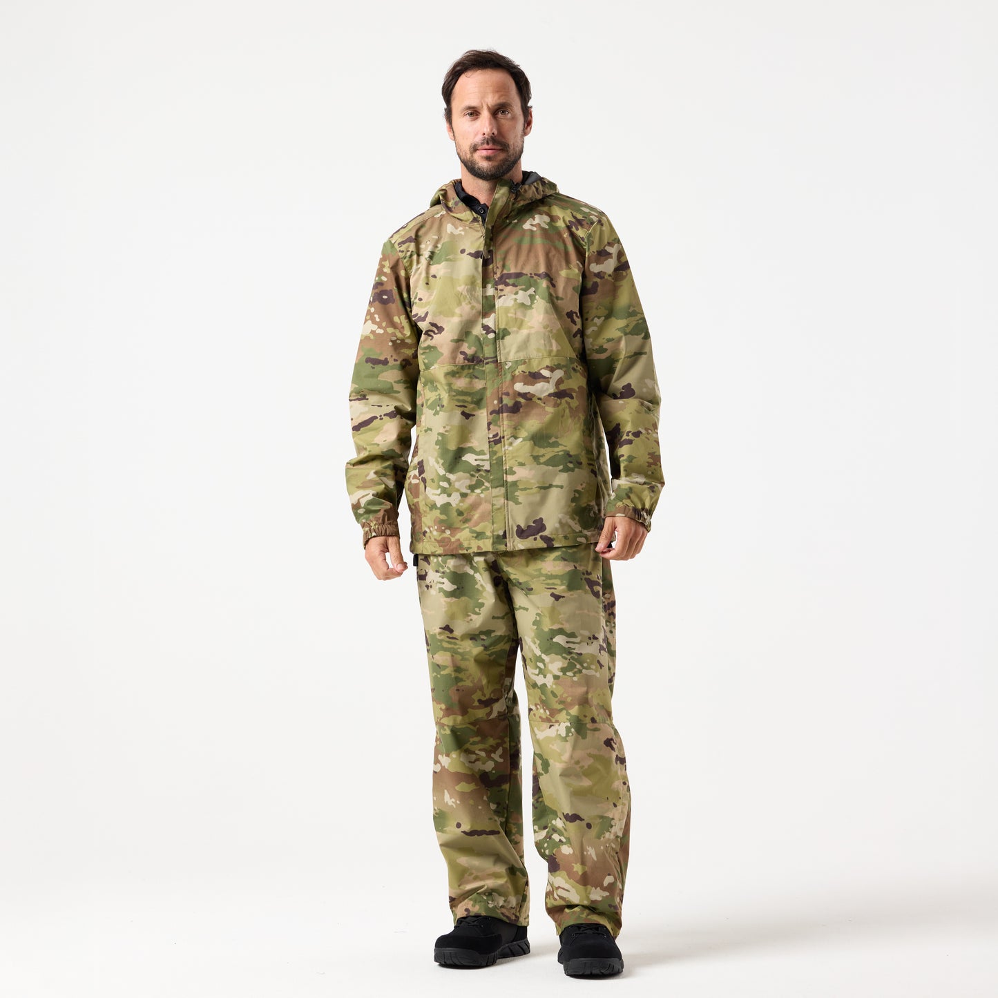 A man stands facing forward against a plain white background, wearing DFND Assault Pants paired with a camouflage jacket and black shoes.