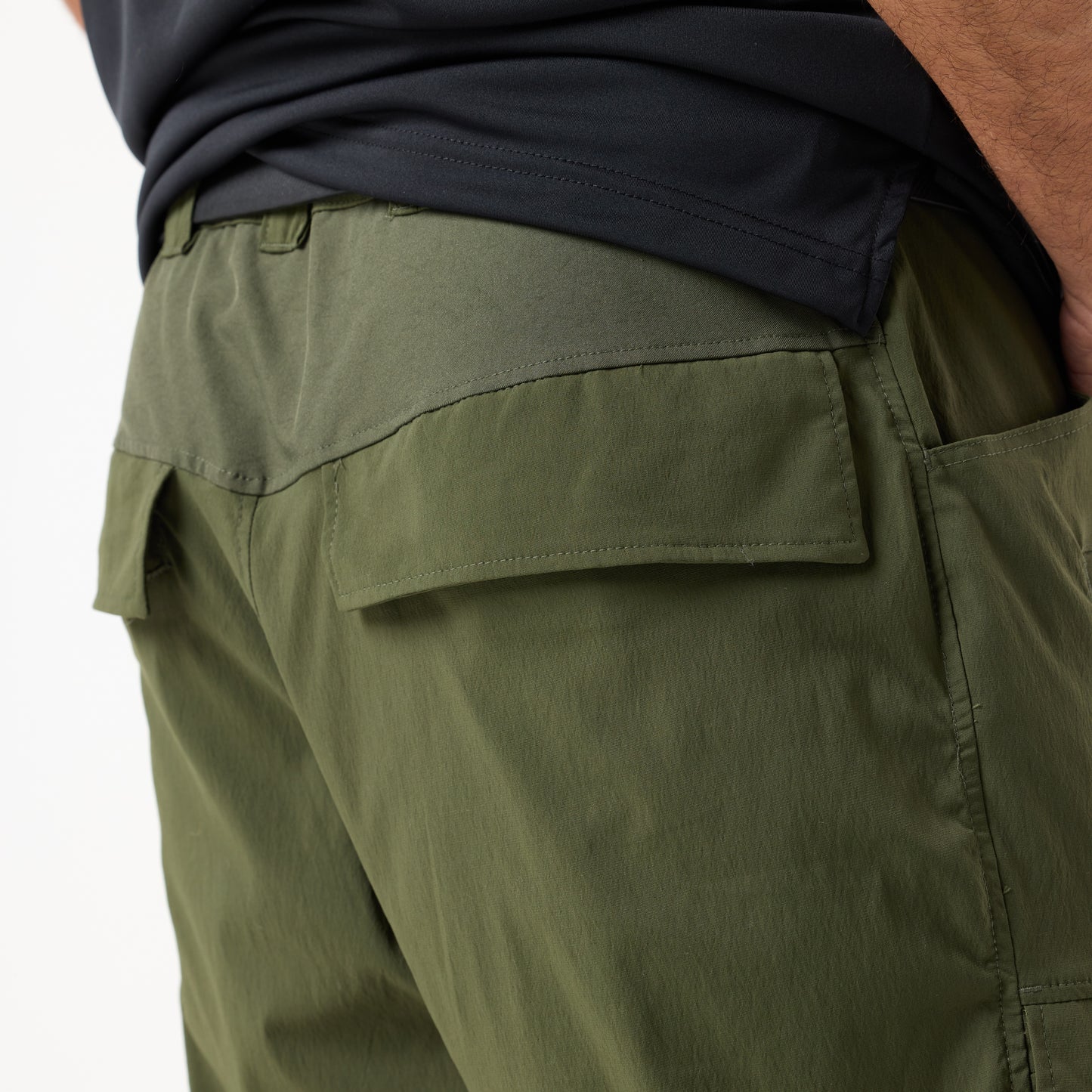 Close-up of a person wearing DFND MISSION CARGO SHORTS in olive green, featuring flap back pockets, paired with a black shirt; back view shown.