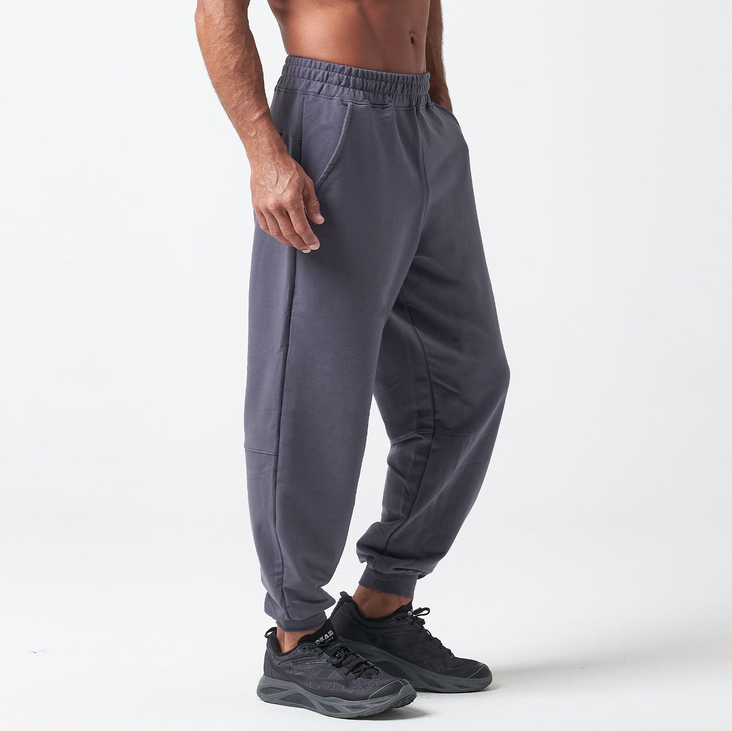 A person wearing charcoal gray joggers and black sneakers stands against a light background.