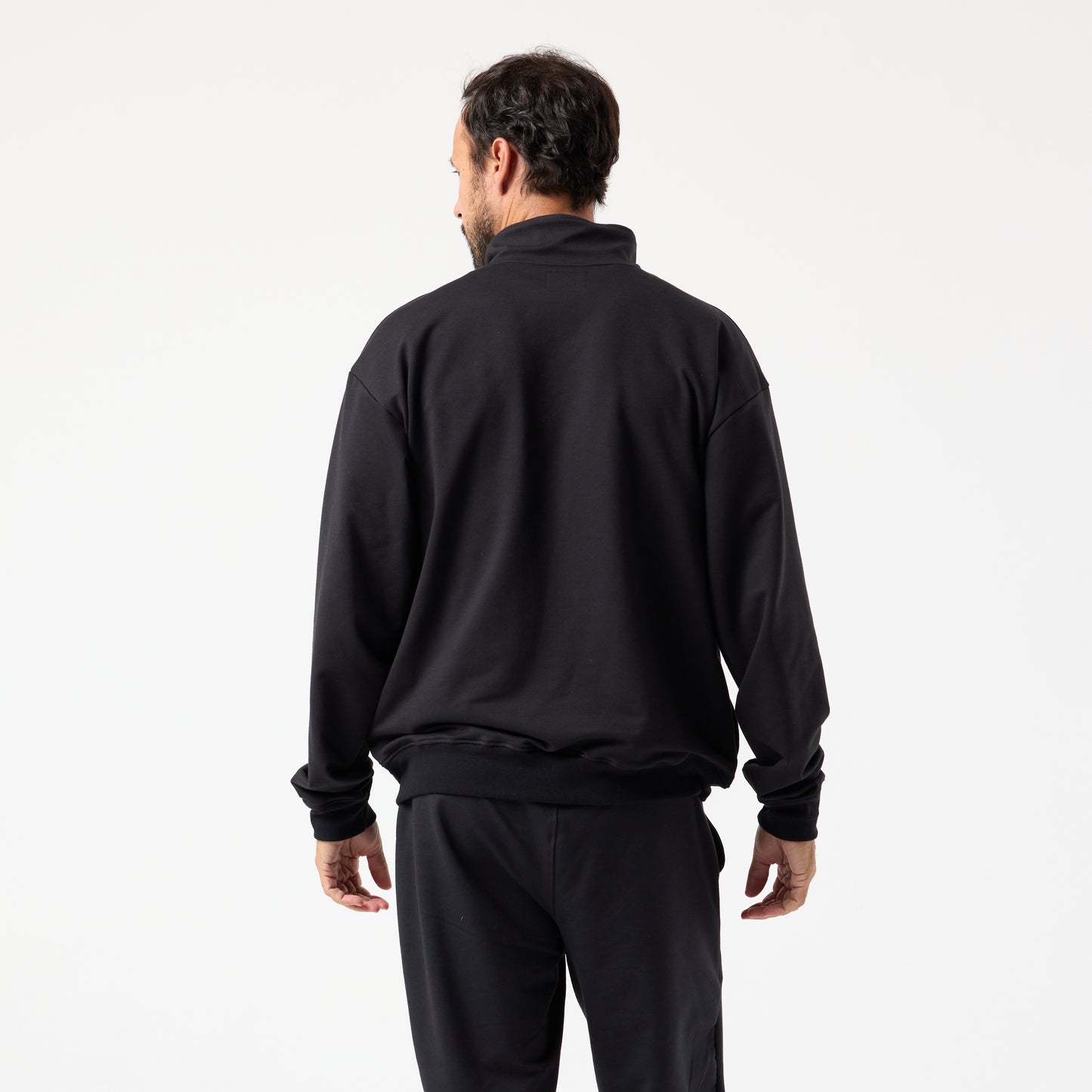 A man faces away from the camera, wearing the DFND IR Travel & Recover 1/4 ZIP sleepwear made with CELLIANT textiles to enhance tissue oxygen, set against a plain white background.