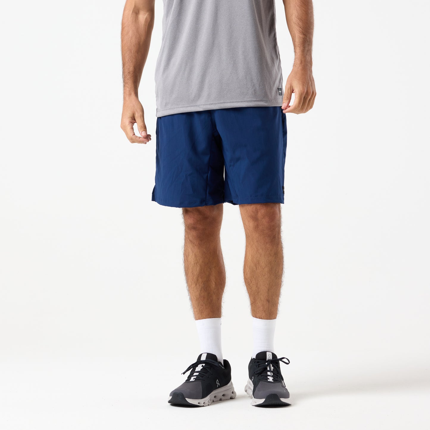 A person wearing a gray T-shirt, DFND MALIBU 9" SHORTS, white socks, and black sneakers stands against a plain white background.