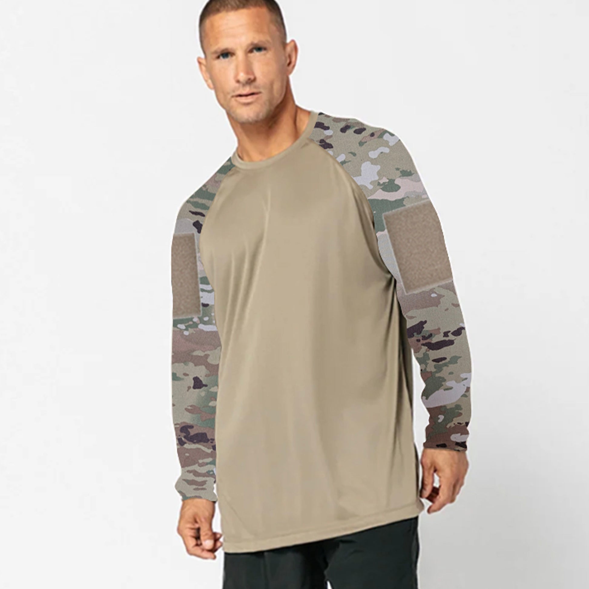 A man wearing a DFND SPEED TECH LS SHIRT WITH VELCRO—beige with camouflage-patterned sleeves—and black pants stands against a plain light background.