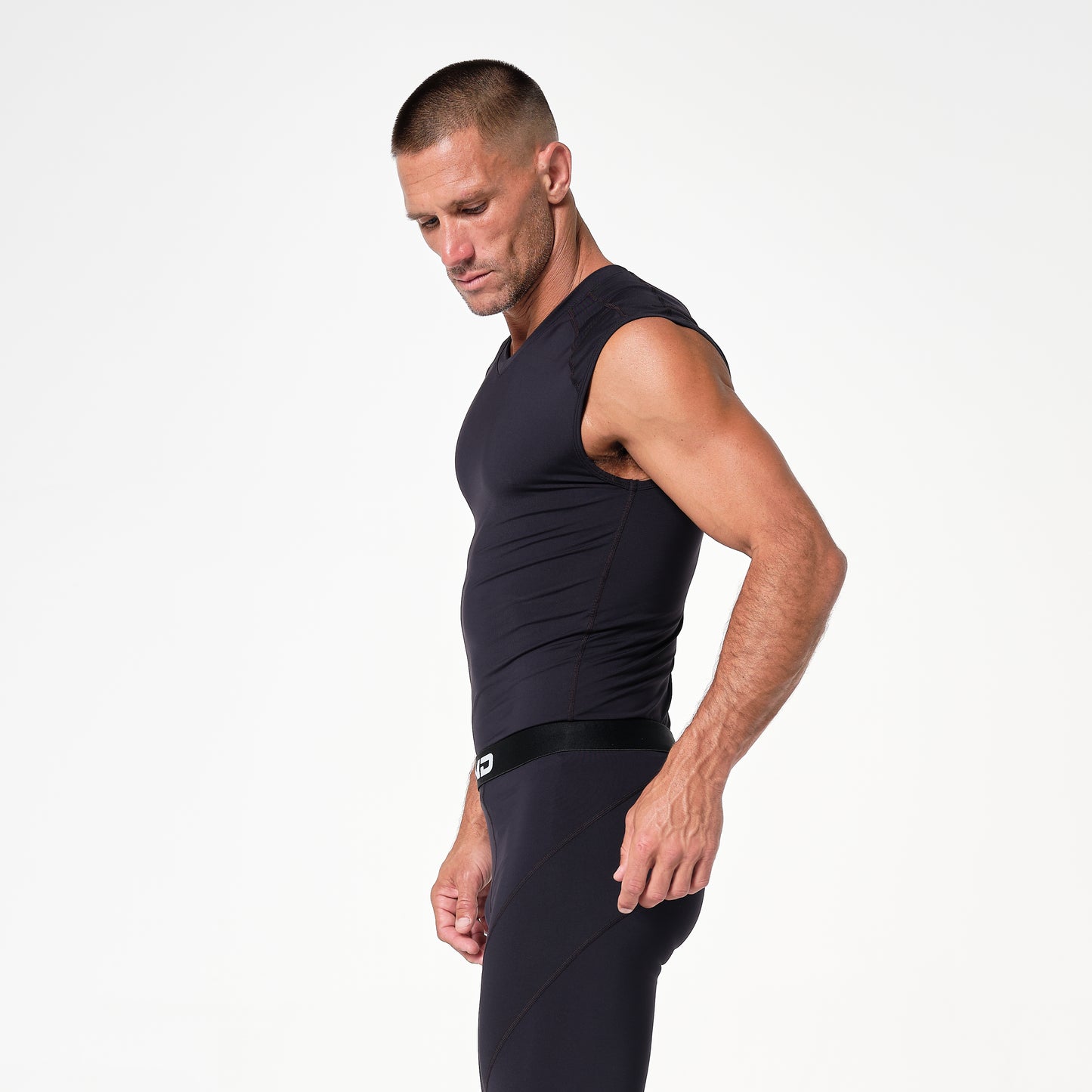 Man in a black sleeveless athletic outfit stands in profile against a plain white background.