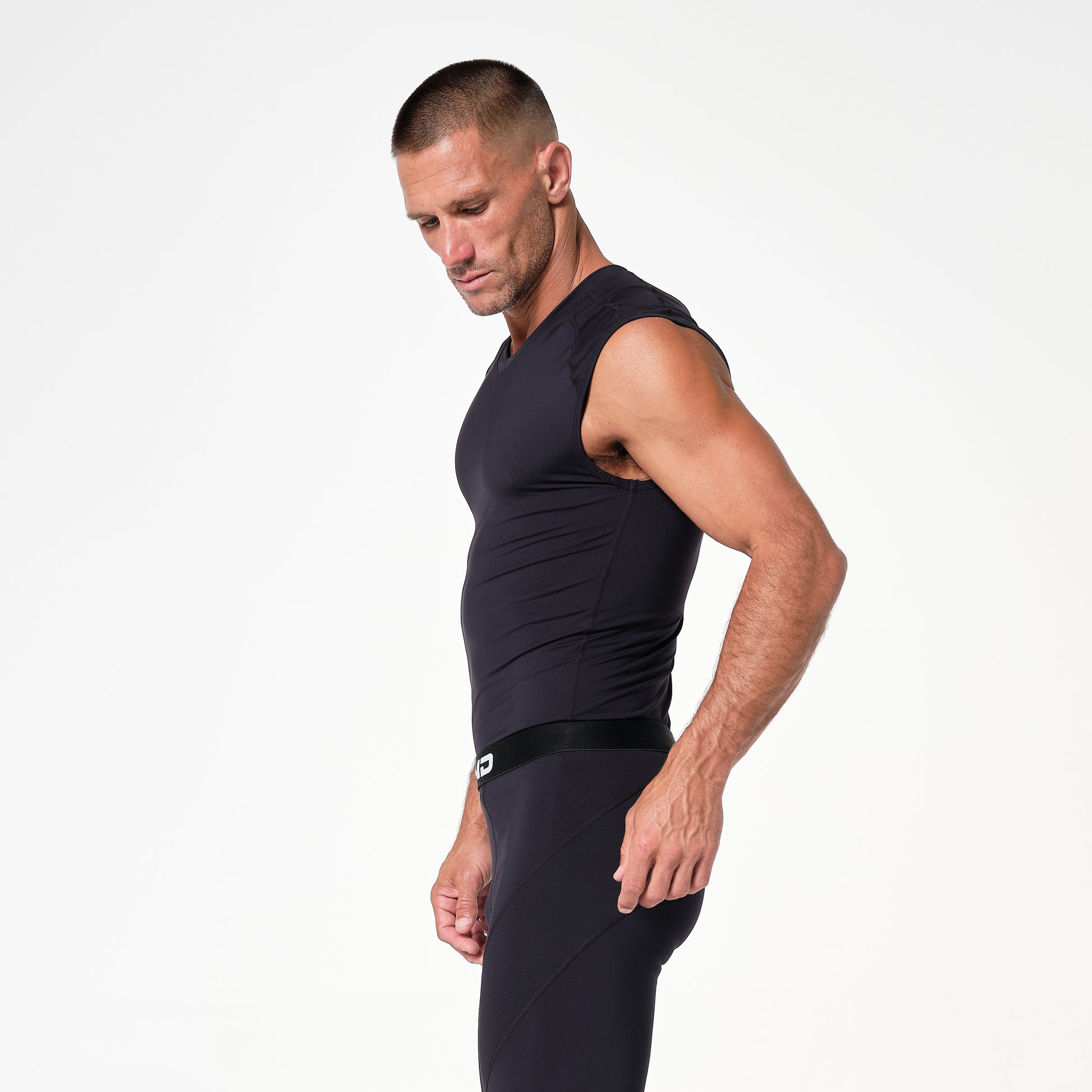 Man in a black sleeveless athletic outfit stands in profile against a plain white background.