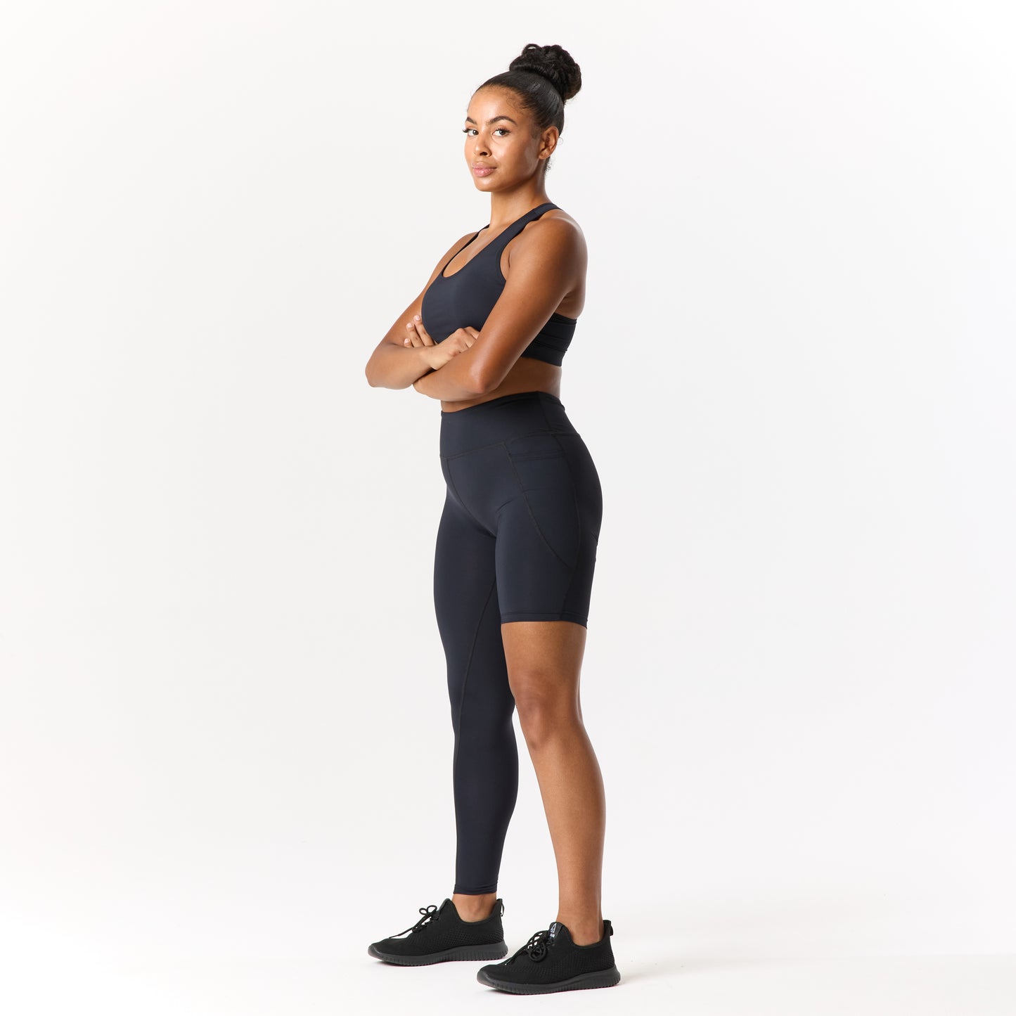 A person in a black sports outfit stands with arms crossed, facing forward against a white background.