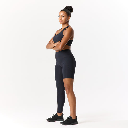 A person in a black sports outfit stands with arms crossed, facing forward against a white background.