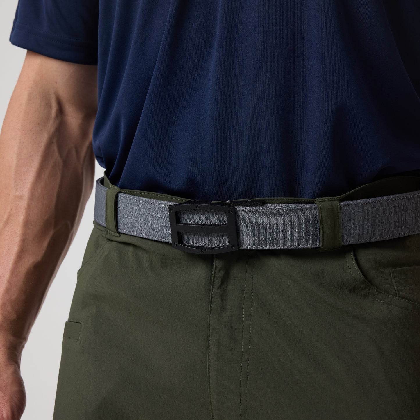 A person wearing a DFND Utility Polo in navy with moisture-wicking fabric, olive green pants, and a gray belt with a black buckle.