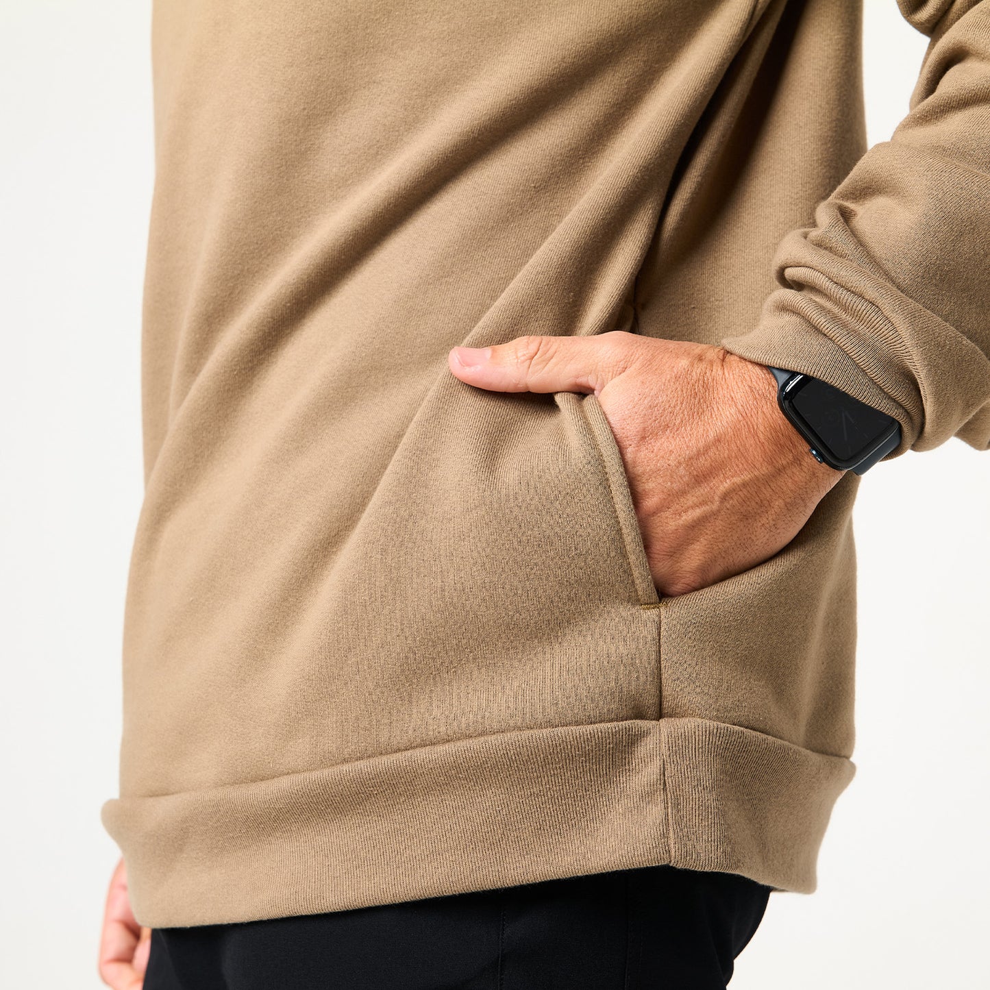 A person wearing a tan long-sleeve shirt and DFND’s Memphis Fleece Hood, with a hand in the side pocket and a black smartwatch, shown side-on—perfect for cold weather training.