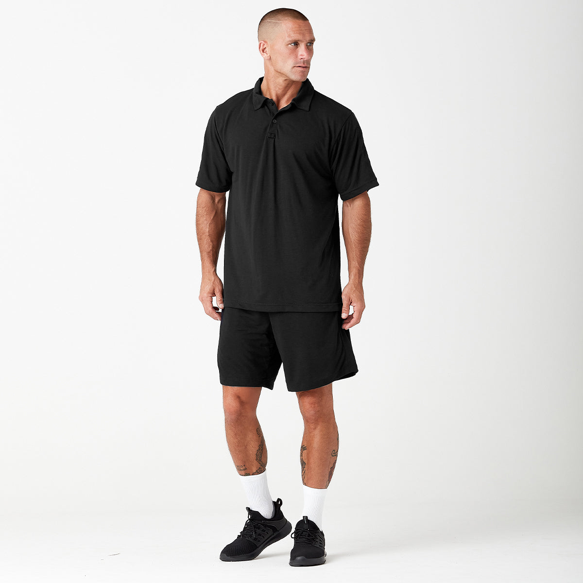 A person wearing a navy blue polo shirt, matching shorts, white socks, and black sneakers stands facing left against a plain white background.