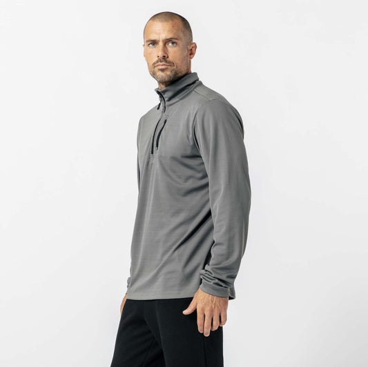 A man wearing a gray long-sleeve zip-up top and black pants stands against a plain white background.