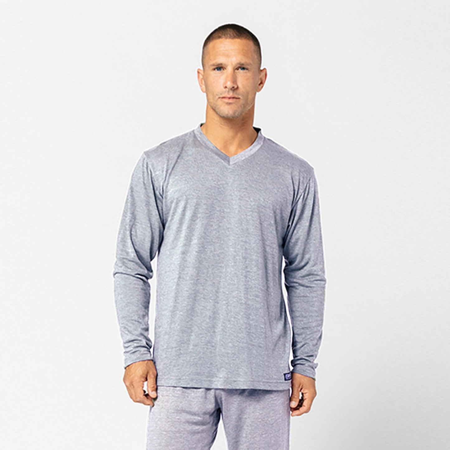 A man stands facing forward against a plain white background, wearing a light gray DFND Cooling Recovery Sleepwear LS Shirt and matching pants, designed with CELLIANT minerals to help improve sleep quality.