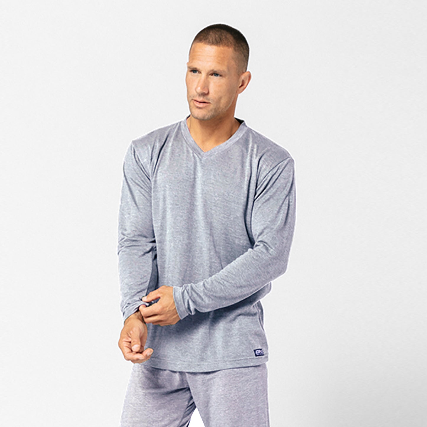 A man wears the DFND Cooling Recovery Sleepwear LS Shirt in light gray along with matching pants, standing against a plain background. This innovative sleepwear by DFND is designed to help improve sleep quality.