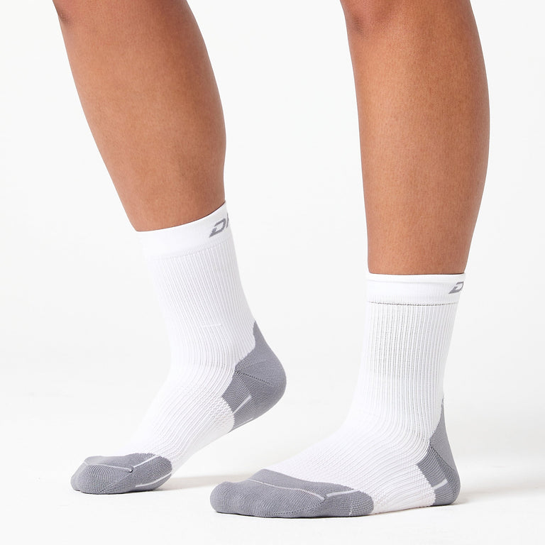 A person wearing white and gray crew socks stands on a white surface, showing the socks from the side and front angles.