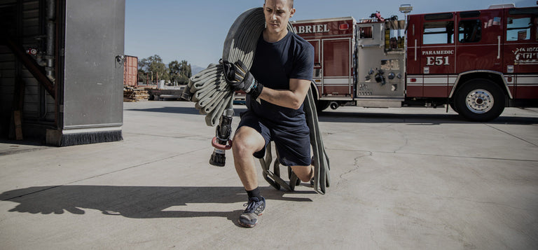 A man wearing gloves and a cap uses a large crowbar to pry open the door of a weathered, metal storage unit or garage.