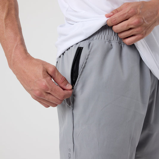 Someone wearing the DFND Speed Tech Hoodie + Aero Short Outdoor Kit in light gray is lifting their white shirt and unzipping the black zipper pocket on the Aero Short.