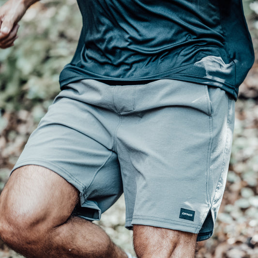 A person wearing a dark shirt and gray DFND AERO SHORT 9″ performance training shorts is mid-stride outdoors, with the focus on the DFND AERO SHORT 9″ shorts and upper legs.