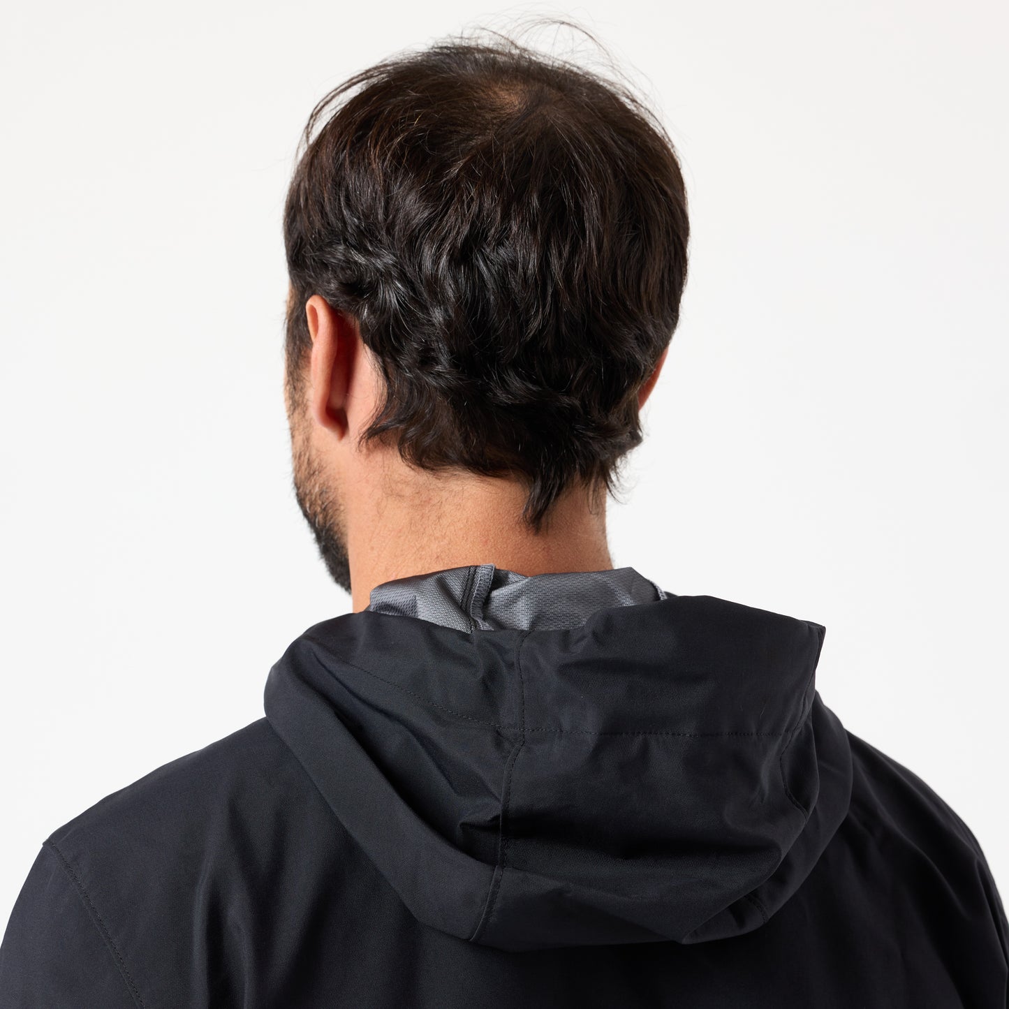 A man with thinning hair is seen from behind wearing the DFND Assault Jacket, a black, lightweight hooded jacket, set against a plain white background.