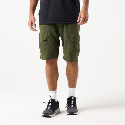 A person wearing a black shirt, DFND MISSION CARGO SHORTS in olive green with zippered cargo pockets, white socks, and black athletic shoes stands against a plain white background.