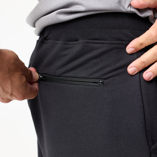 A person’s hand pulls the zipper on the side hip pocket of DFND’s IR Travel & Recover Rx Jogger in black.