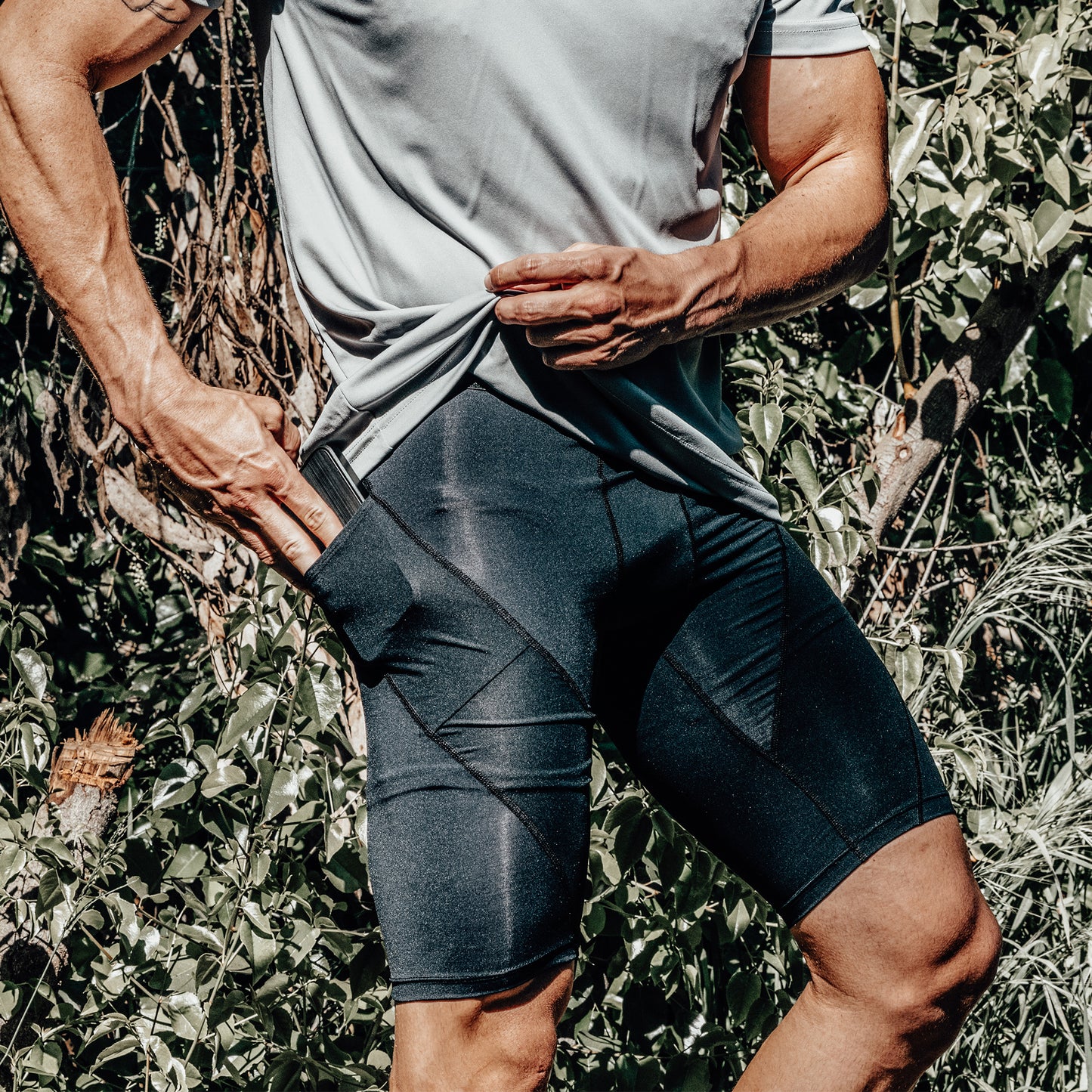 While outdoors, a person tugs at the pocket of their DFND Active Ax Compression Shorts, highlighting the functional pocket detail and emphasizing both contemporary style and reliable pelvic stability.