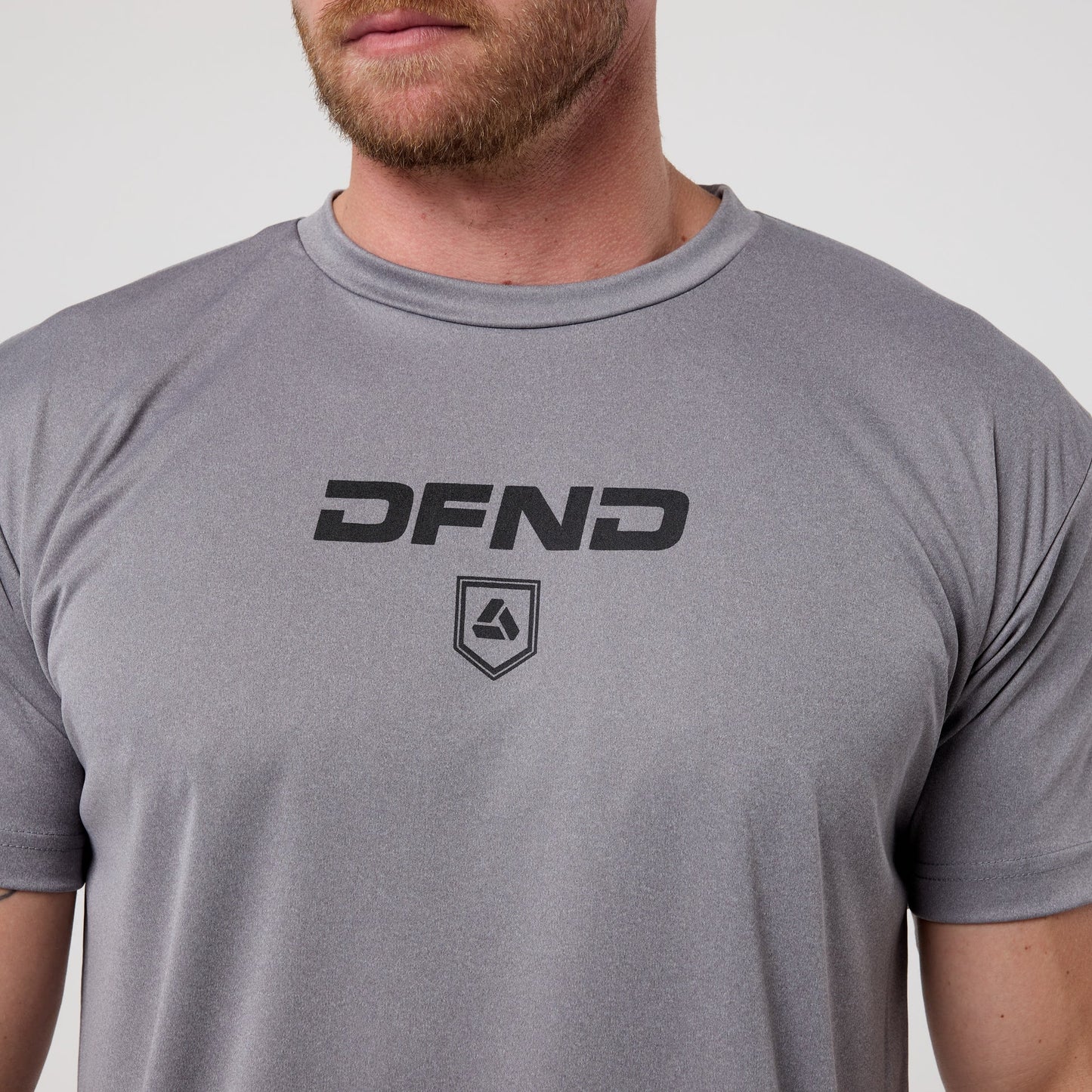 A person with a short beard wears the DFND Speed Tech Short Sleeve from the Aero Short Outdoor Kit, featuring the DFND logo and emblem on quick-drying fabric—perfect for outdoor performance.