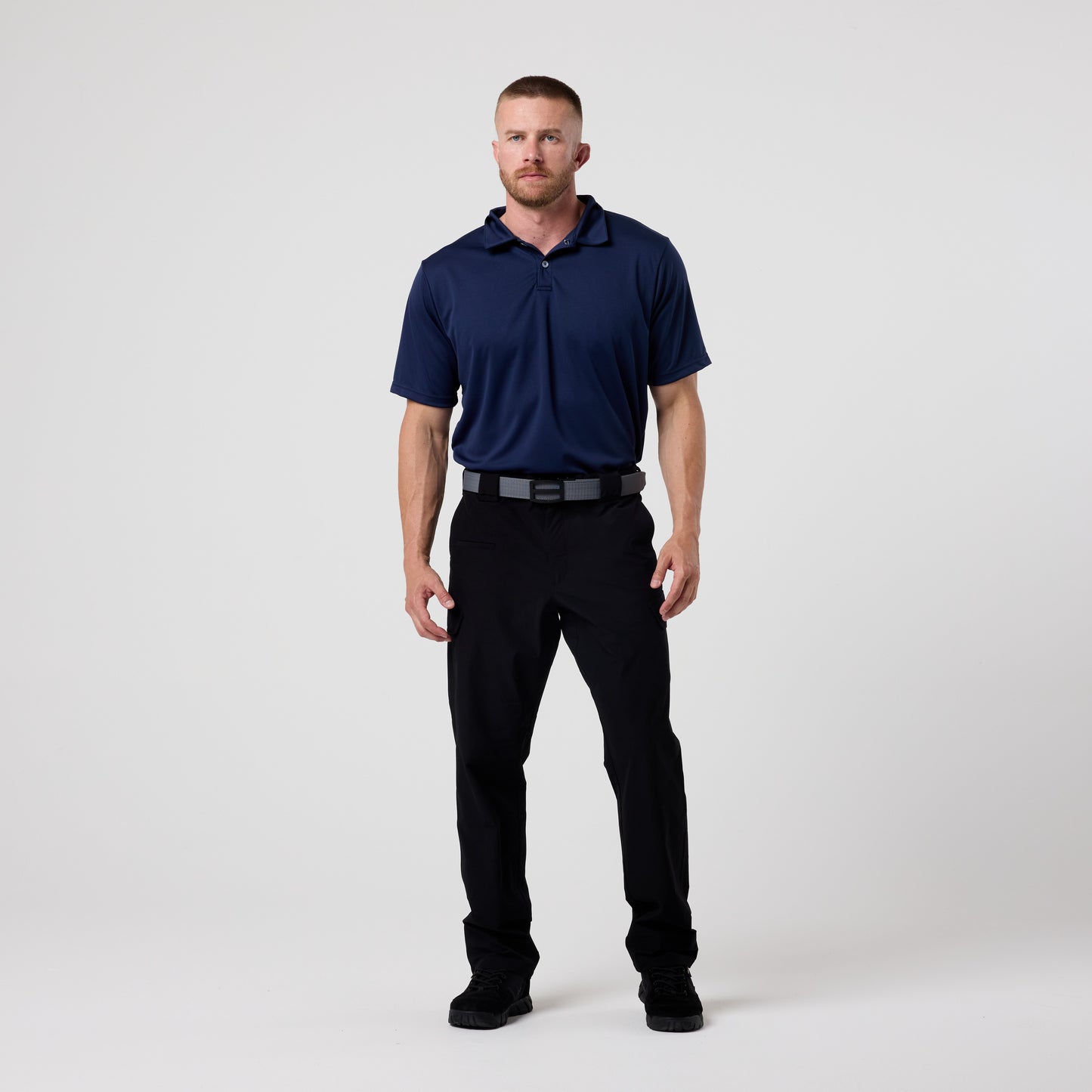 A man stands facing forward against a plain white background, wearing the DFND GALAXY PERFORMANCE POLO with SPF50+ protection, paired with black pants and black shoes.