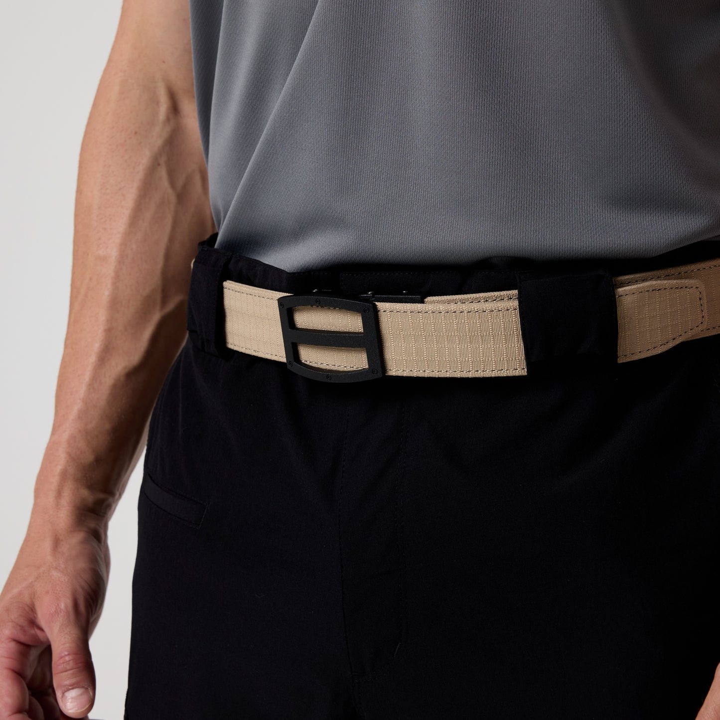 A person wearing a DFND GALAXY PERFORMANCE POLO in grey, featuring moisture-wicking fabric, paired with black pants and a tan belt with a black rectangular buckle. Only the torso and part of the right arm are visible.