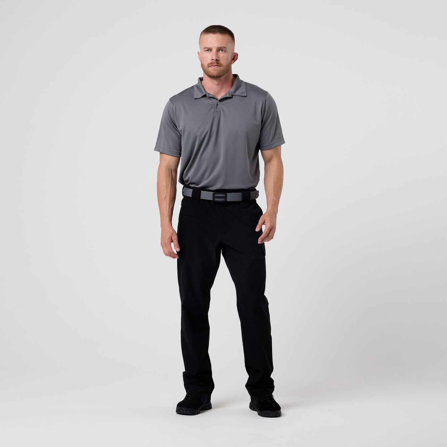 A man stands facing forward in a gray DFND GALAXY PERFORMANCE POLO with SPF50+ protection, paired with black pants and black shoes, against a plain white background.
