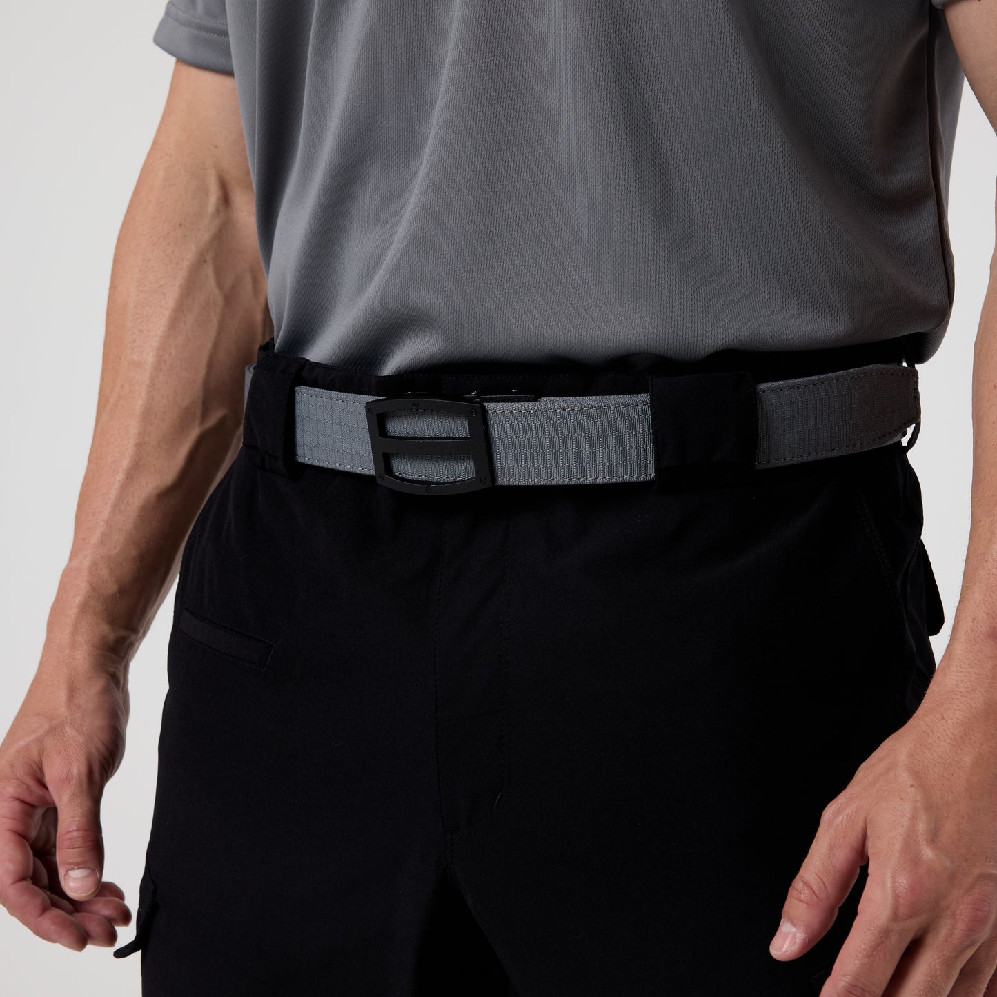 A person wearing a gray DFND GALAXY PERFORMANCE POLO, black pants, and a gray tactical belt with a rectangular buckle.