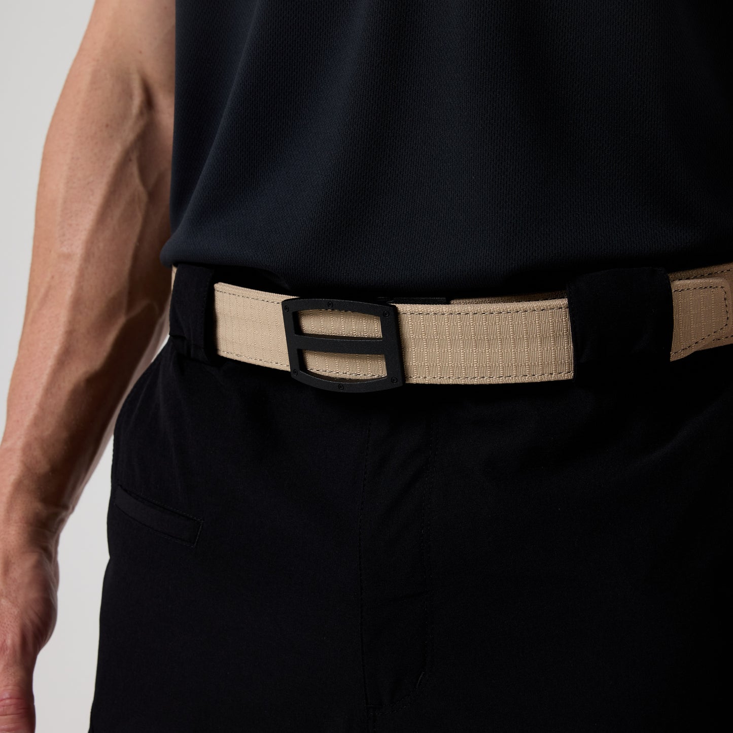 A person wearing the DFND GALAXY PERFORMANCE POLO in black with moisture-wicking fabric, black pants, and a beige belt featuring a rectangular black buckle.