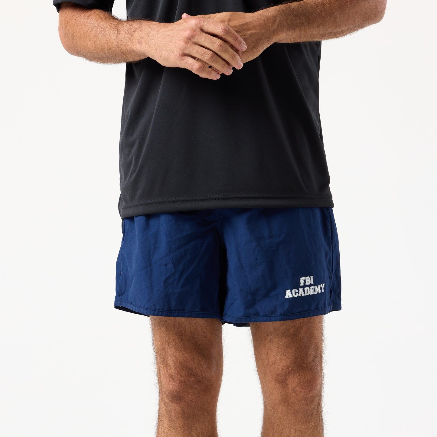 A person wears a black shirt and DFND MALIBU 5" PT SHORTS FBI ACADEMY, featuring "FBI Academy" on the left leg, and stands against a plain white background.