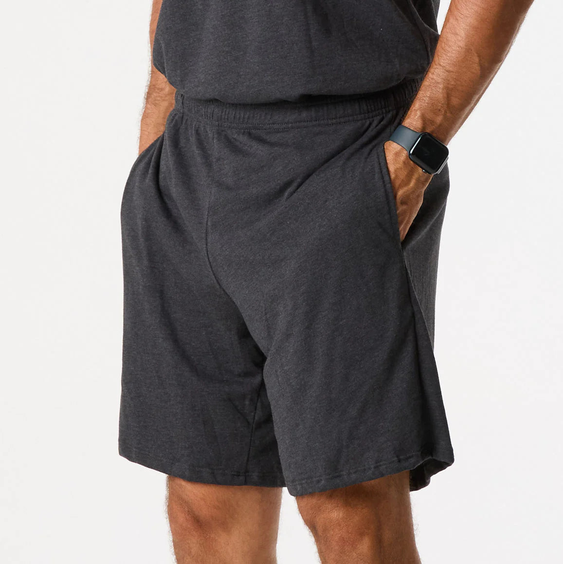 A person models the DFND Sleepwear SS Shirt & Shorts in dark gray, featuring CELLIANT-powered infrared recovery technology for comfort, shown from shoulders to knees with hands in pockets.