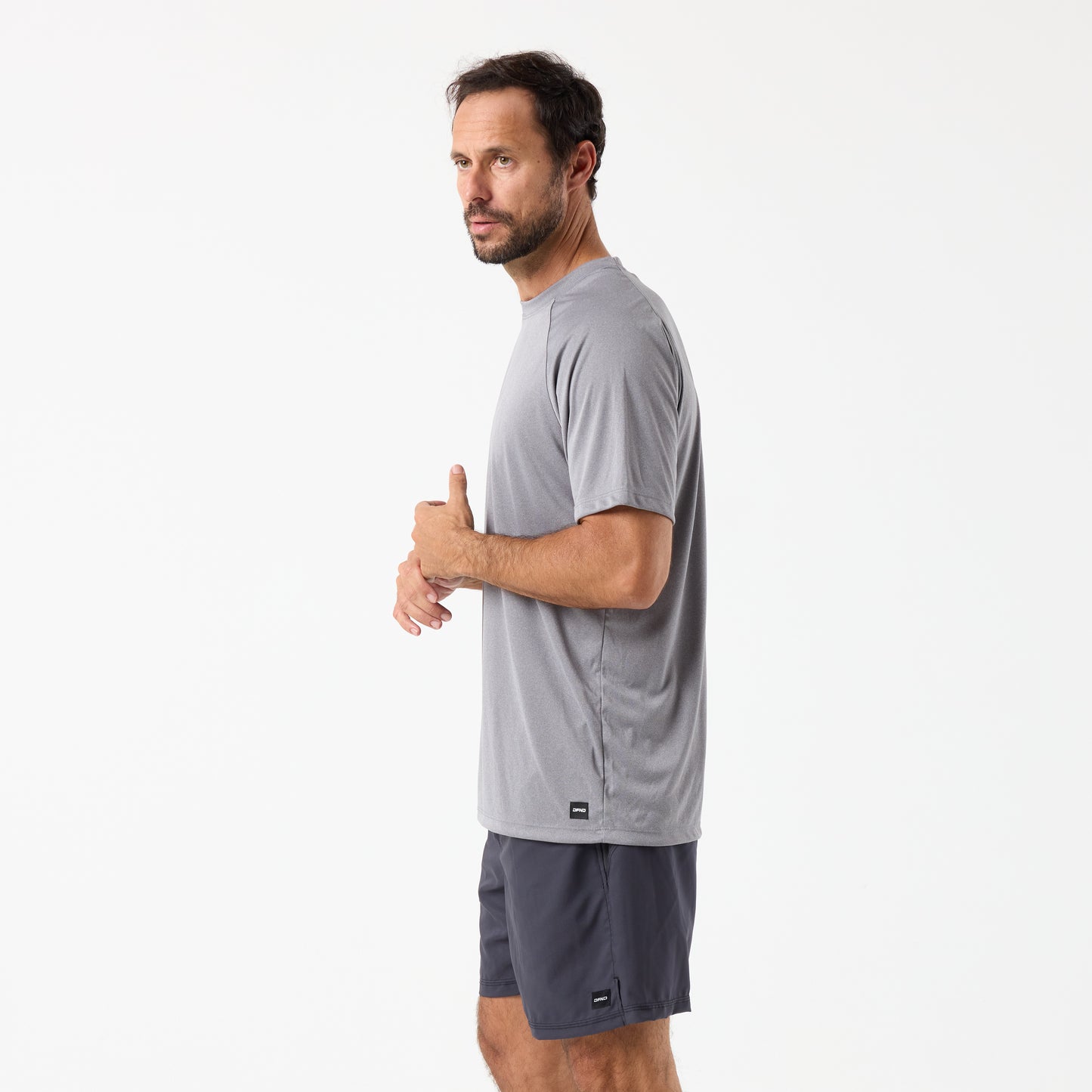 A man in a gray DFND SPEED TECH SS SHIRT with raglan sleeves, made from FUZE antimicrobial fabric, and dark gray shorts stands against a plain white background, facing slightly to the side.