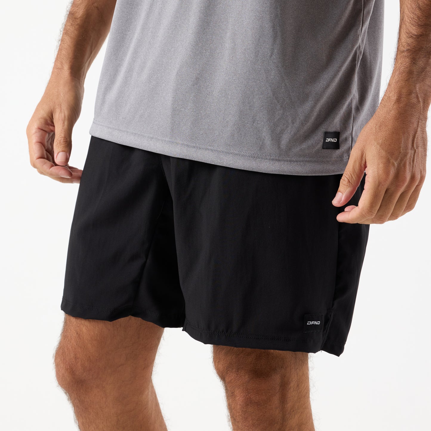 A person wears a grey DFND SPEED TECH SS SHIRT - Raglan Sleeve with moisture-wicking properties and black athletic shorts, shown from waist to mid-thigh against a plain background.