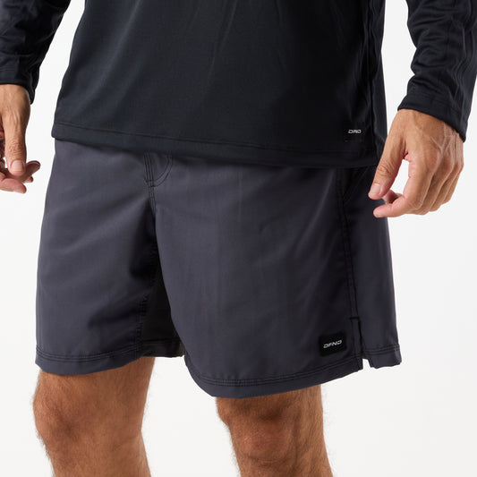 A person wearing the DFND SPEED TECH LS SHIRT with raglan sleeves in black and dark gray shorts stands with their arms slightly bent at their sides.