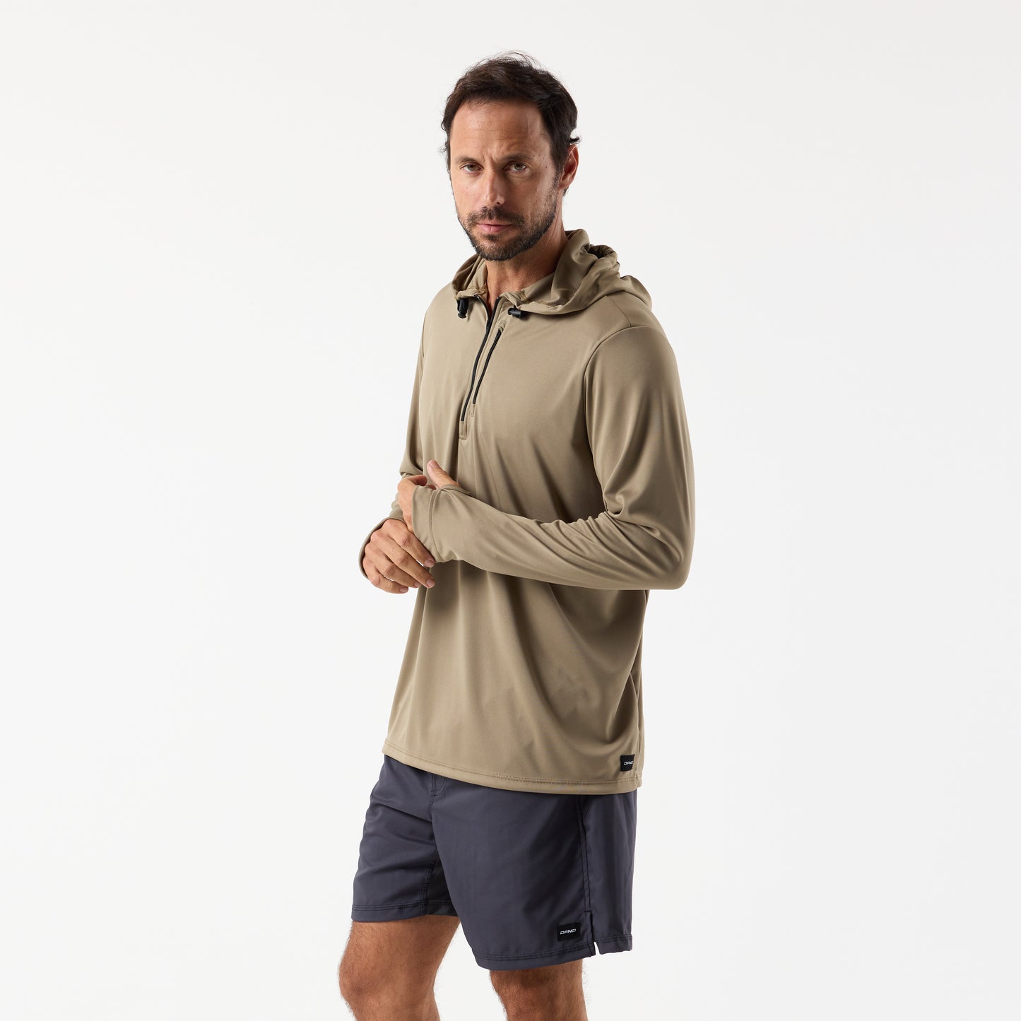 A man wearing the DFND SPEED TECH HOODED 1/4 ZIP in light brown with SPF 50+ protection and dark shorts stands against a plain white background.