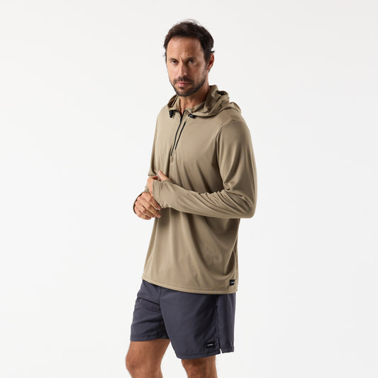 A man wearing the DFND SPEED TECH HOODED 1/4 ZIP in light brown with SPF 50+ protection and dark shorts stands against a plain white background.