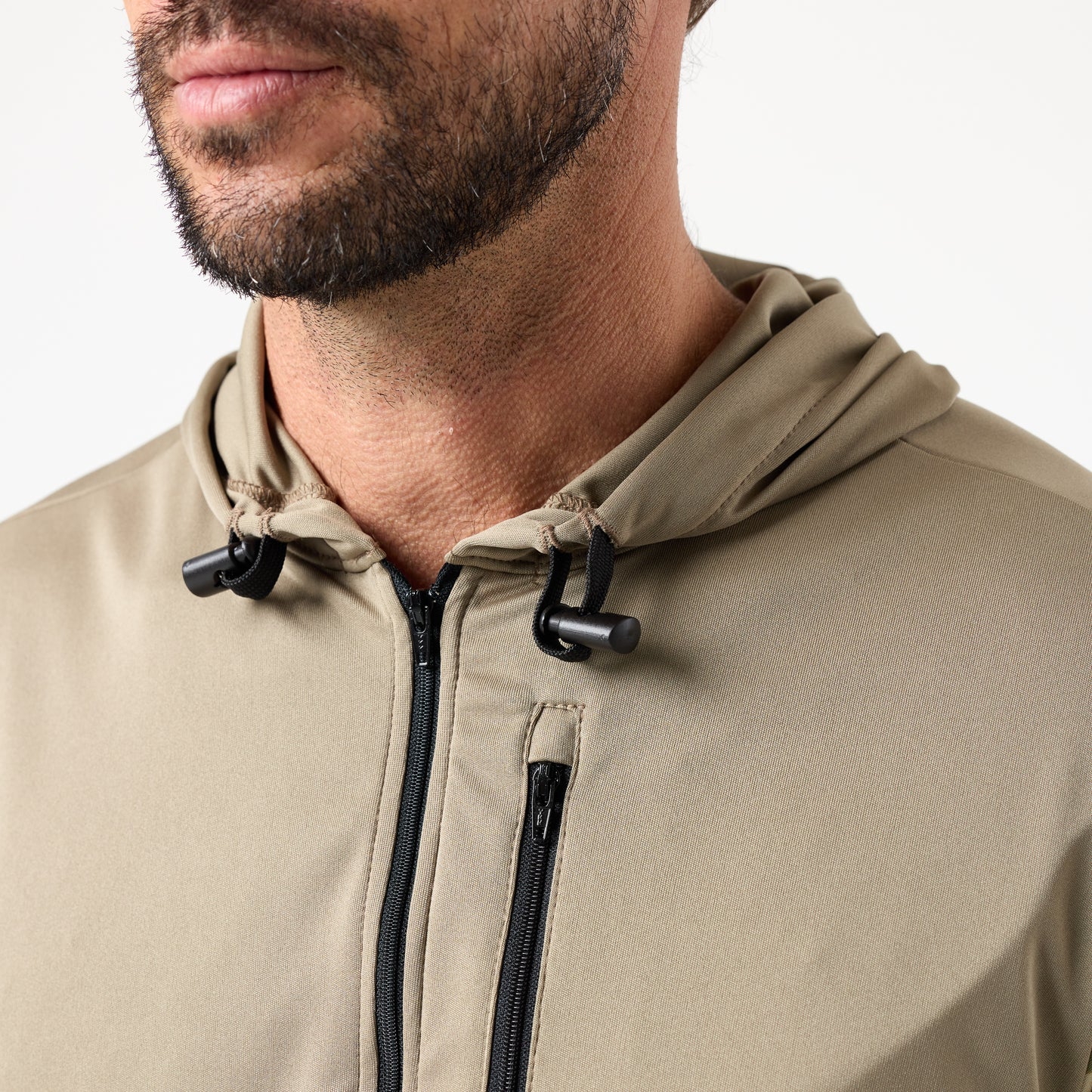Close-up of a man wearing the DFND SPEED TECH HOODED 1/4 ZIP—a light brown pullover with drawstrings, a zippered chest pocket, and moisture-wicking, antimicrobial fabric for lasting comfort.