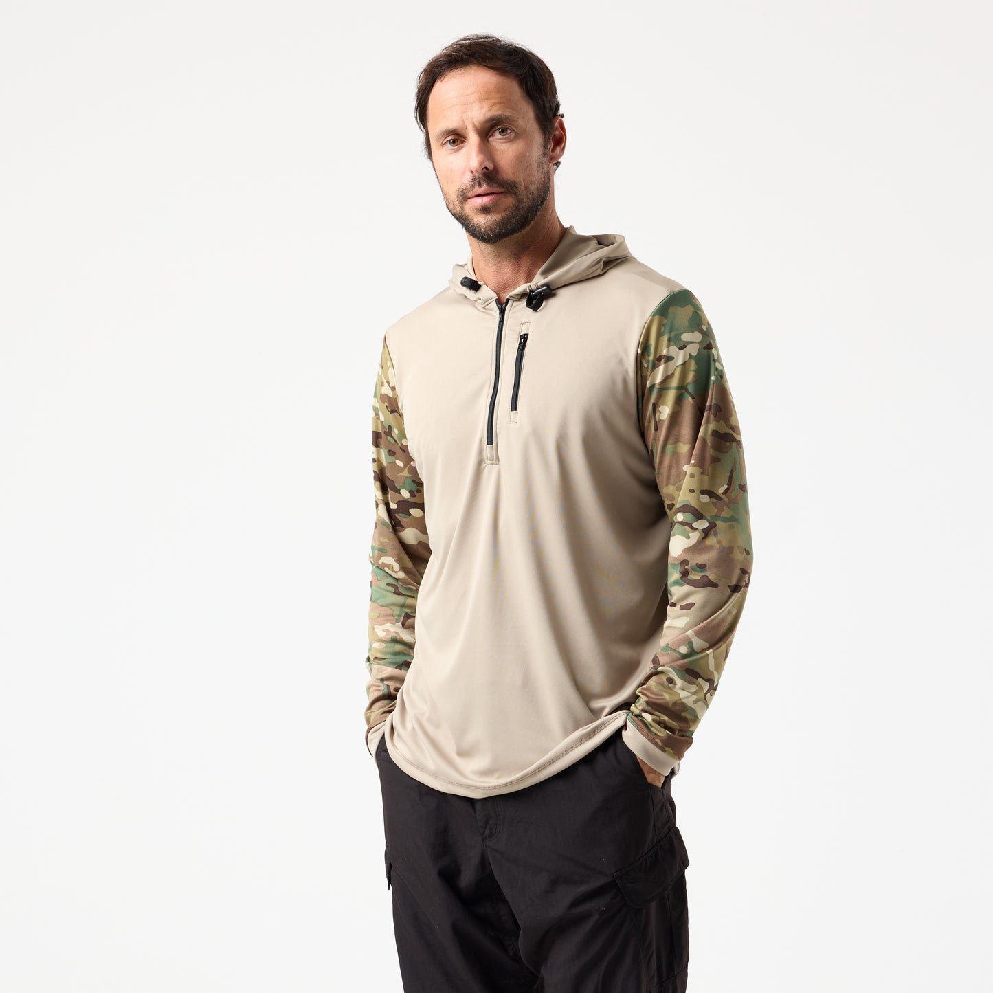 A man stands against a plain background wearing the DFND SPEED TECH HOODED 1/4 ZIP in beige with camouflage sleeves and black pants, hands in his pockets.