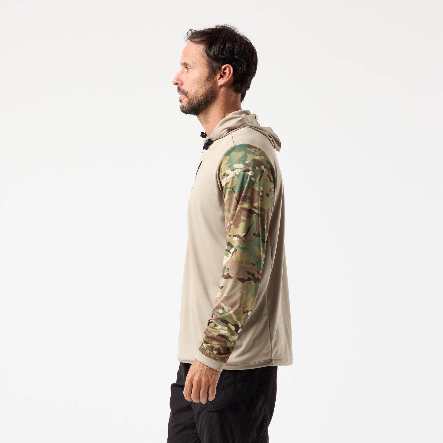 A man in profile wears the DFND SPEED TECH HOODED 1/4 ZIP, a tan hoodie with camouflage sleeves made from antimicrobial fabric, and black pants, standing against a plain white background.