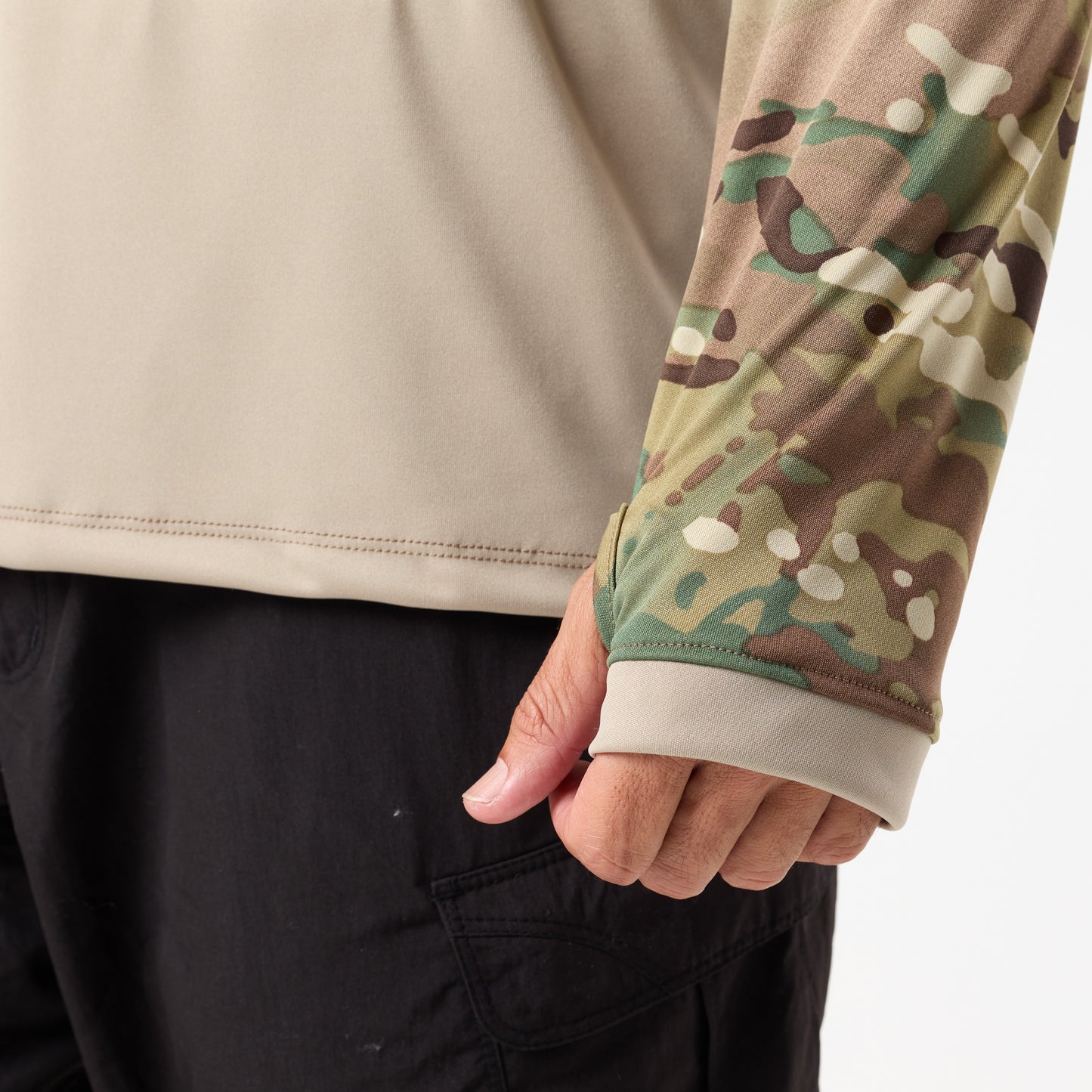 A person wearing black pants and the DFND SPEED TECH HOODED 1/4 ZIP, a beige long-sleeve antimicrobial shirt with a camouflage-patterned sleeve.