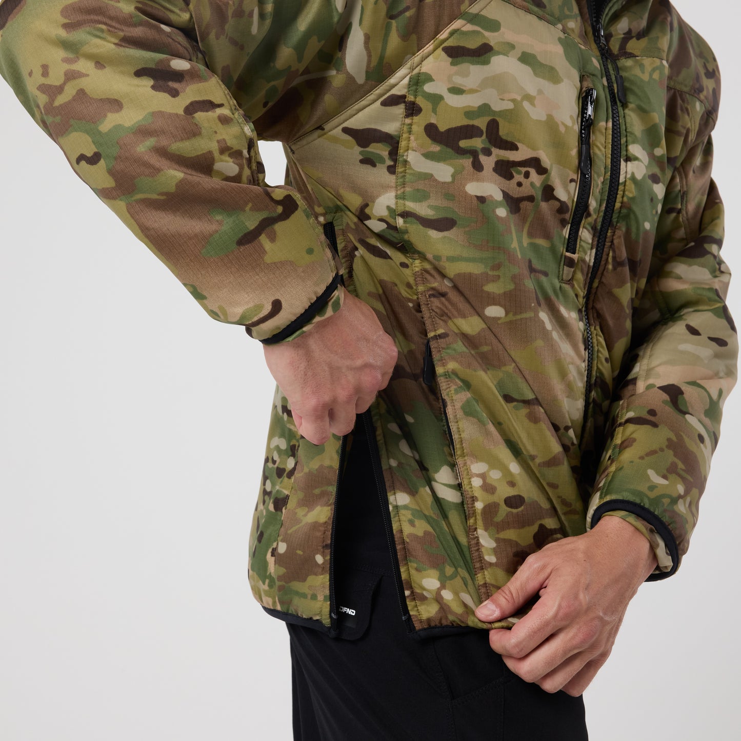 A person in a DFND Warrior Insulated Jacket with a DWR shell is unzipping a side pocket, their torso and arm visible against a plain background.