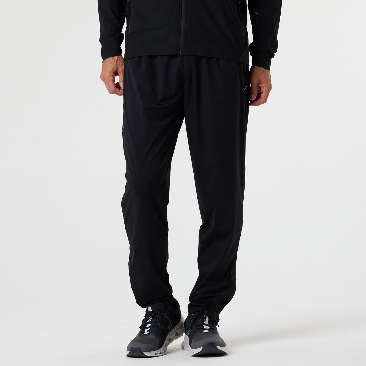 A person wearing DFND FLASH TECH PANTS made from Quick Dry fabric, paired with a black jacket and black and white running shoes, stands against a plain white background.