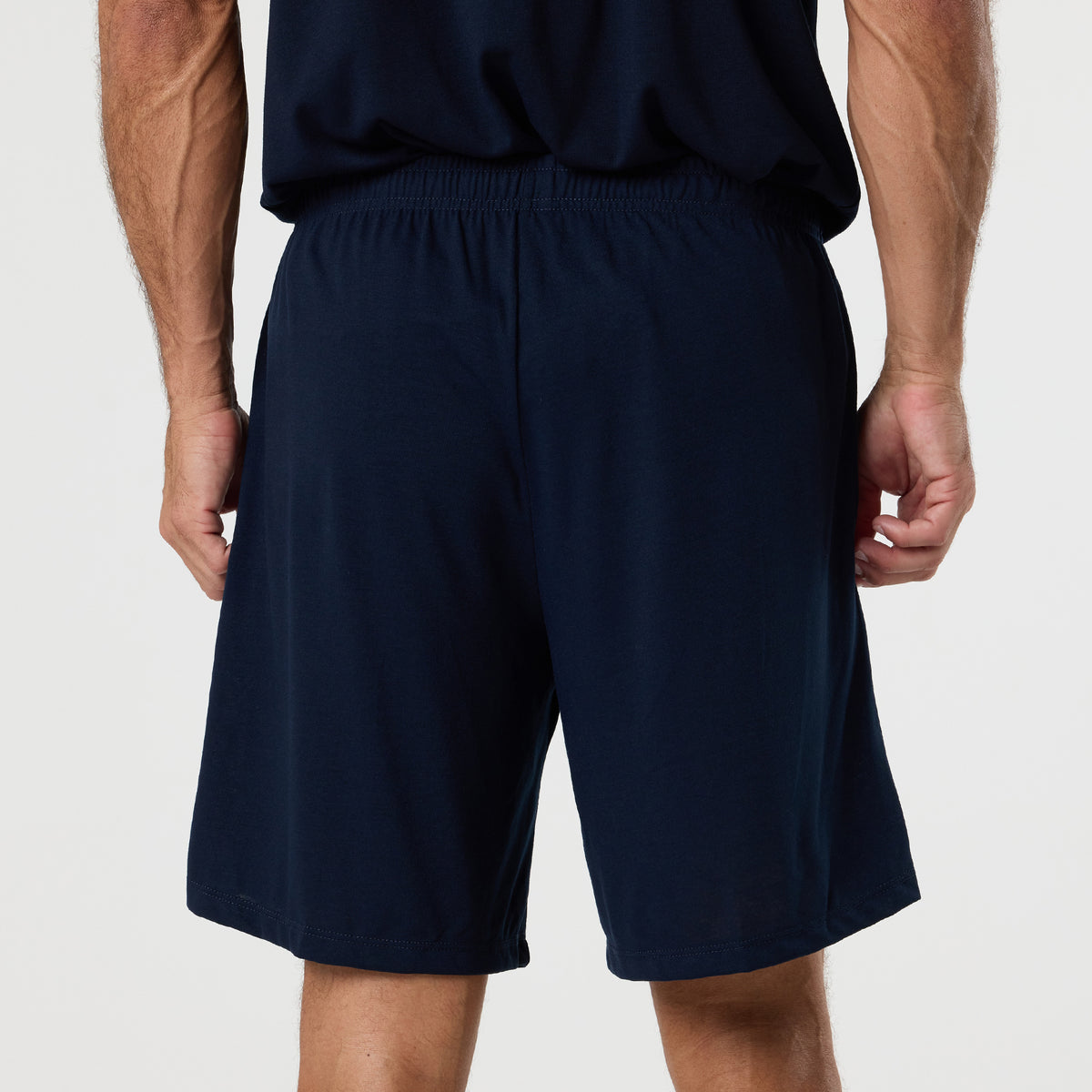 A person standing with their back to the camera, wearing a DFND FR PERFORMANCE SS SHIRT - Traditional Sleeve in navy blue and matching navy blue shorts.