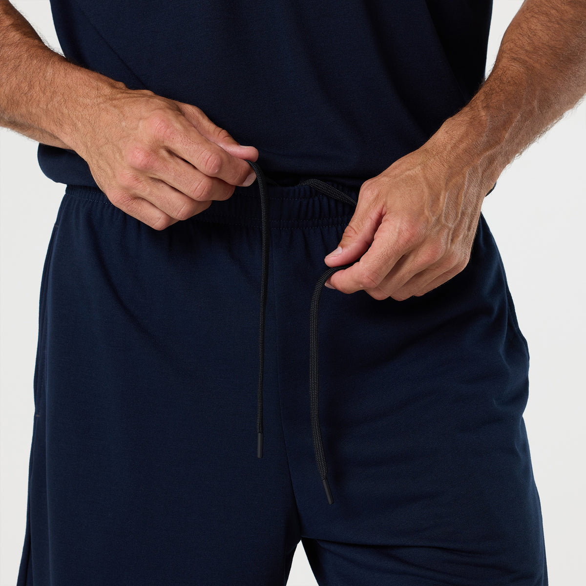 Wearing the DFND FR PERFORMANCE SS SHIRT - Traditional Sleeve in dark blue, a person secures the drawstring on matching pants—an essential combination for today’s fire department uniform.
