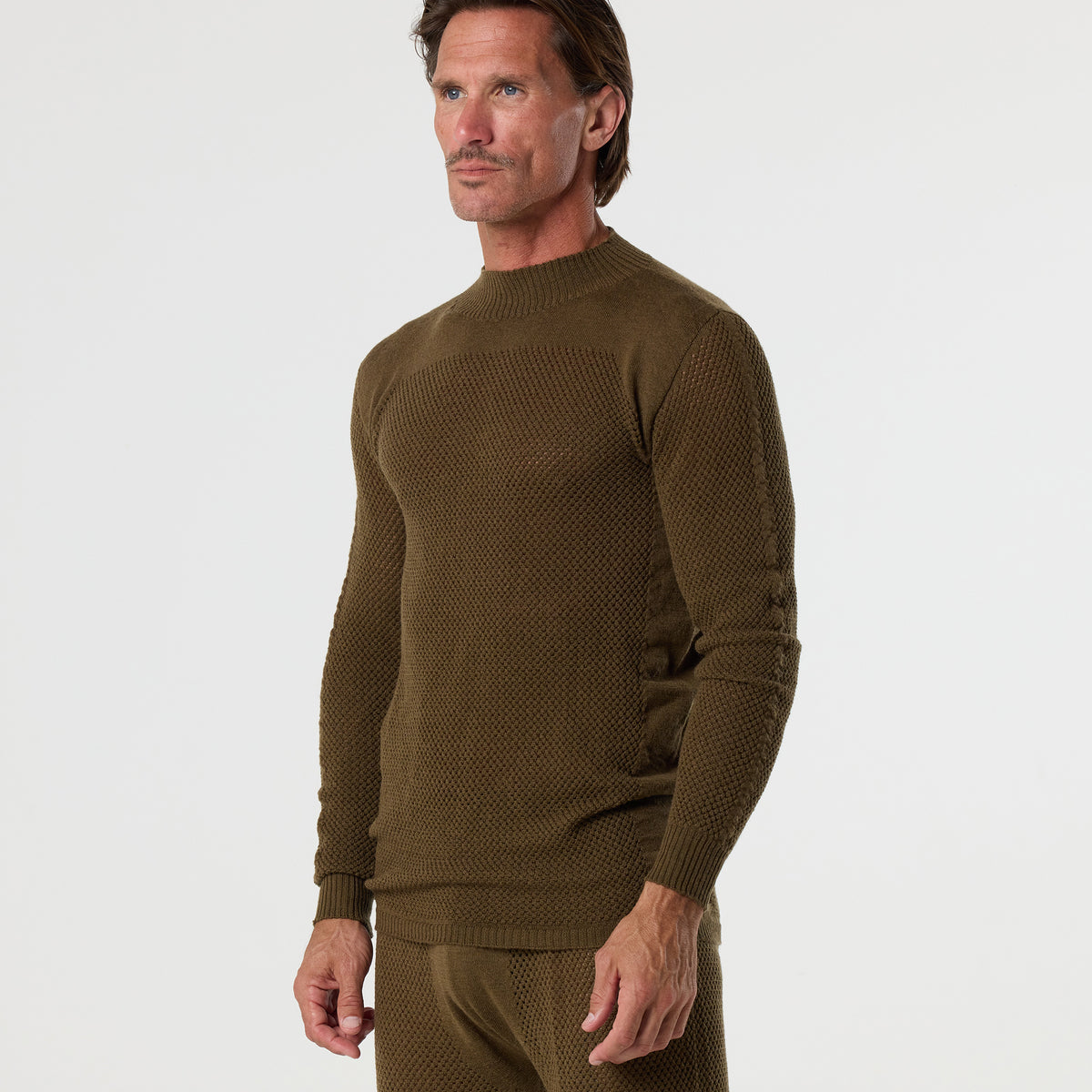 A man stands against a plain background wearing the DFND TAHOE WOOL MESH LONG SLEEVE SHIRT and matching pants, designed for cold weather performance. He looks slightly to the side, showcasing an outfit that offers superior moisture management and comfort.