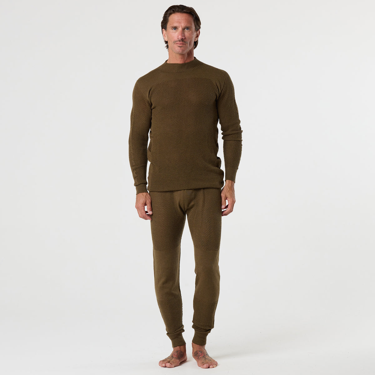 A man stands barefoot on a white background, wearing the DFND TAHOE WOOL MESH LONG SLEEVE SHIRT and matching bottoms, a set designed for superior cold weather performance.