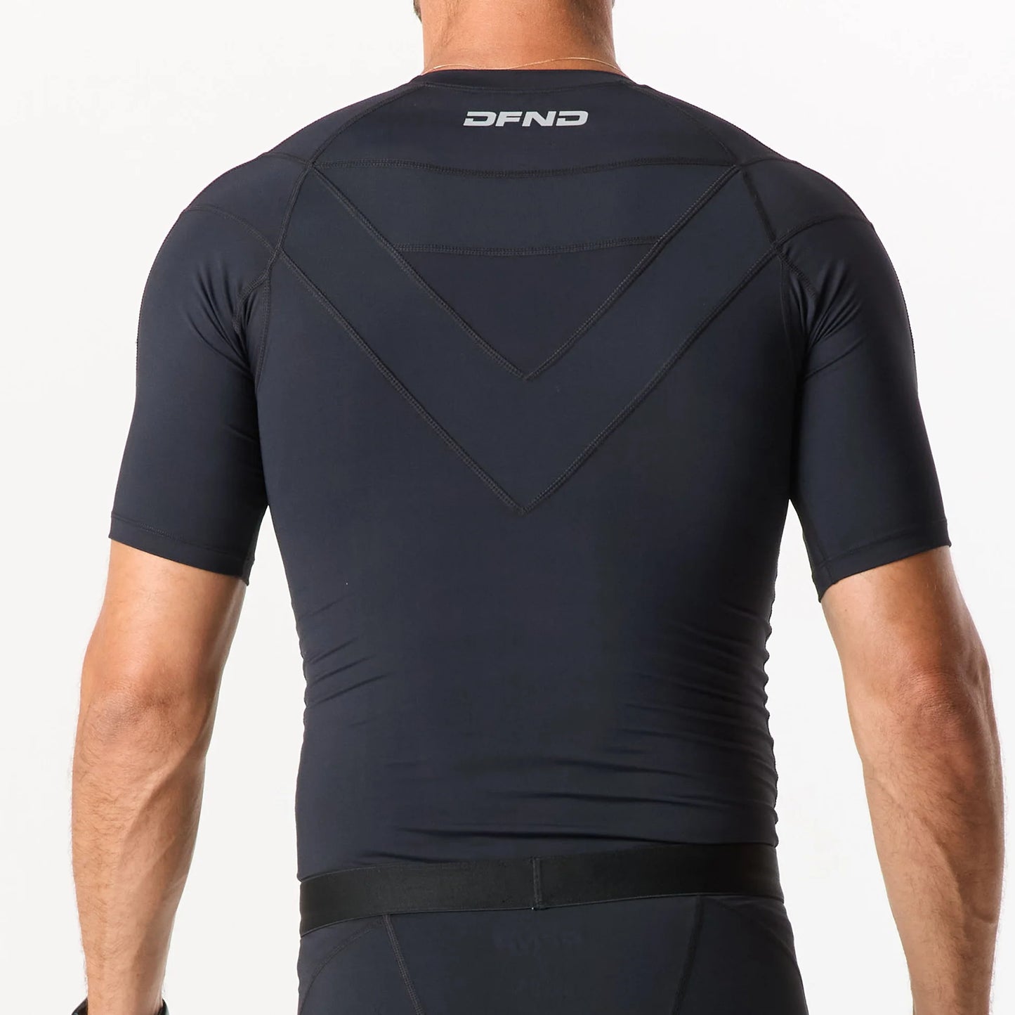 Someone wearing a fitted black short-sleeve athletic shirt, seen from the back with "DFND" near the top—a sleek piece from the DFND Compression Short + Shirt Gym Kit.